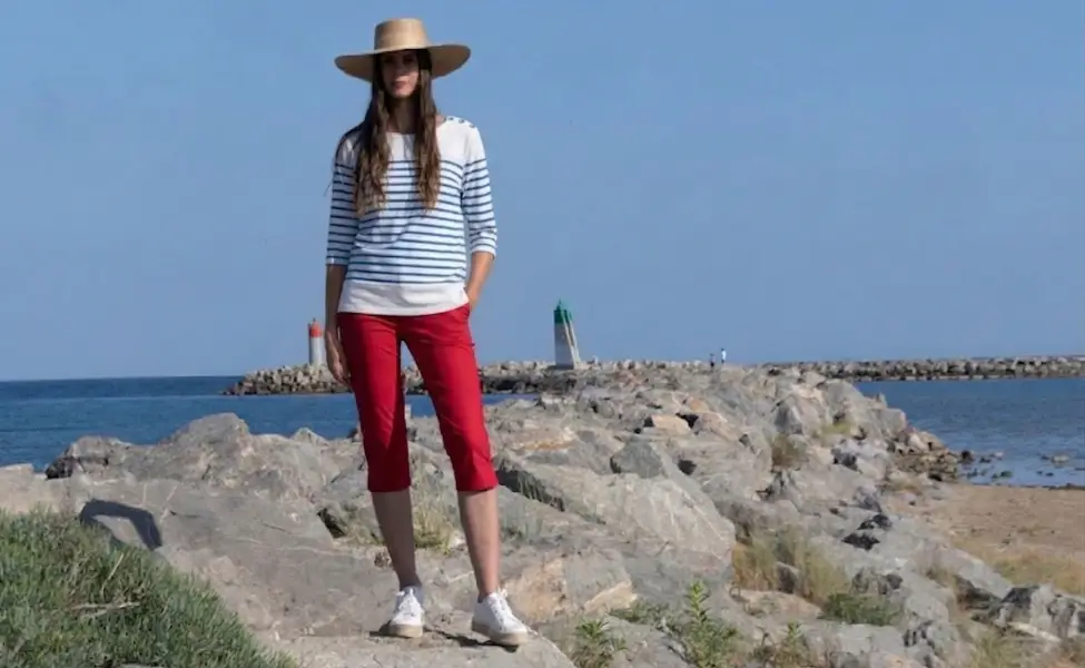 Une femme portant une marinière bastingage blanche rayures à bleu sur une côte rocheuse.